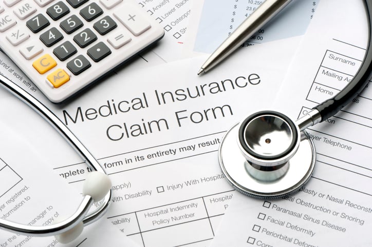 Medical insurance claim forms scattered on a surface with a calculator, a pen, and a stethoscope.